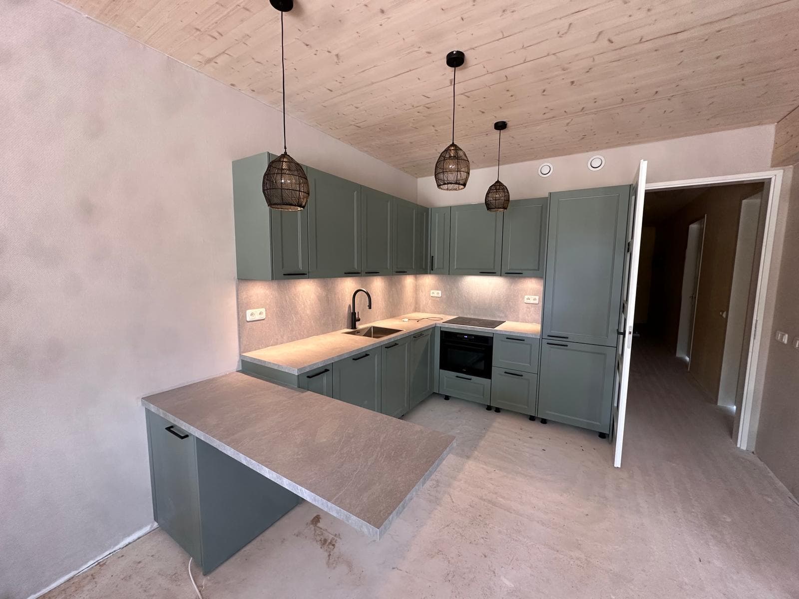 Saliegroene keuken in hoekopstelling met betonlook werkblad en rieten hanglampen