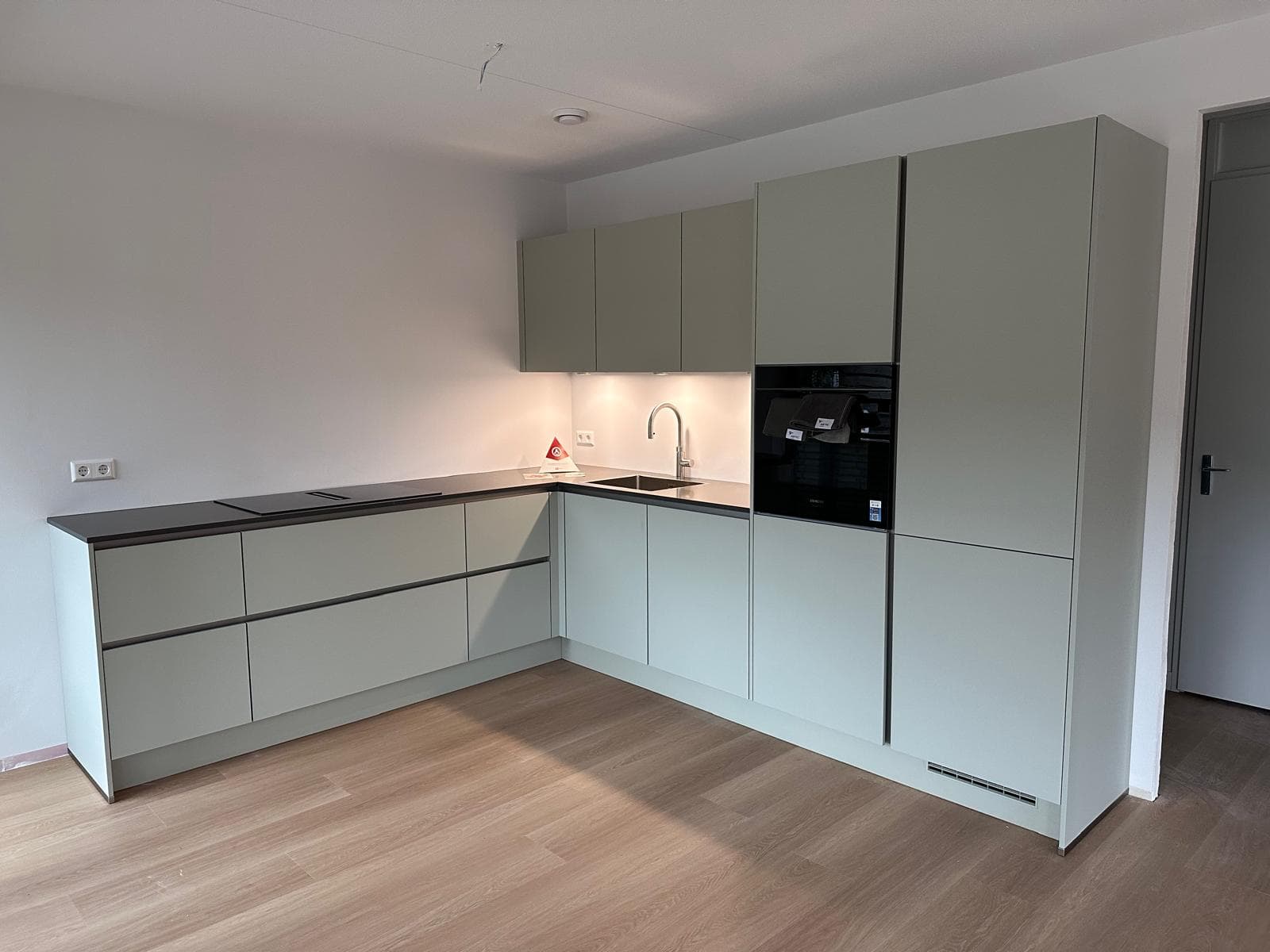Saliegroene keuken met zwart werkblad en zwarte grepen